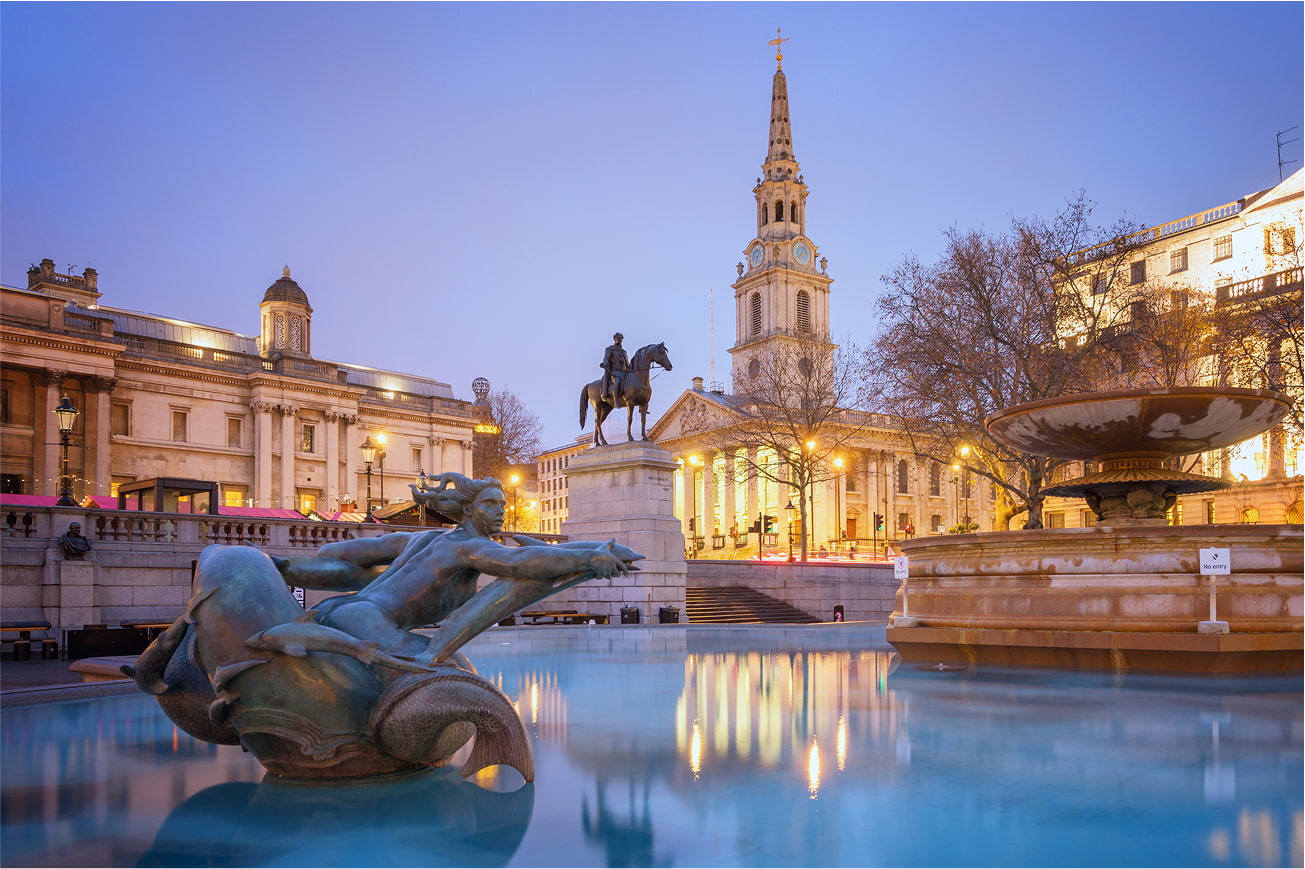 Trafalgar Square fountain and buildings at dusk.