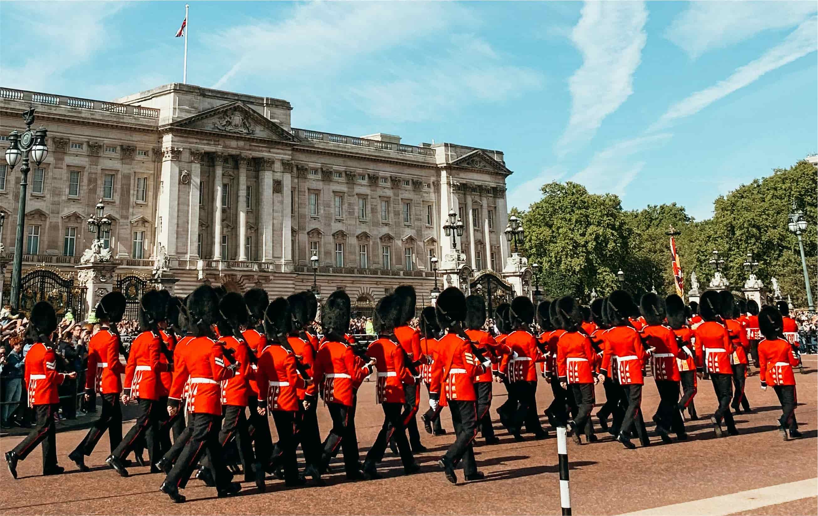 Guards march outside Buckingham Palace in red uniforms.