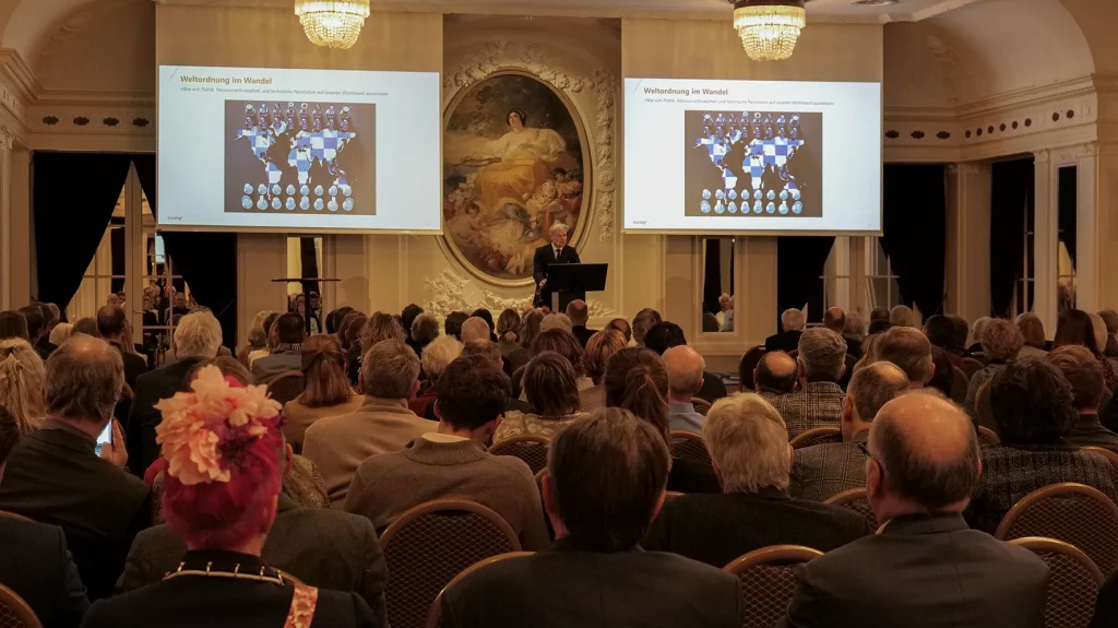 Lecture audience in a grand hall with presentation slides.